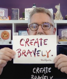 A person holding a sign that reads "Create Bravely".